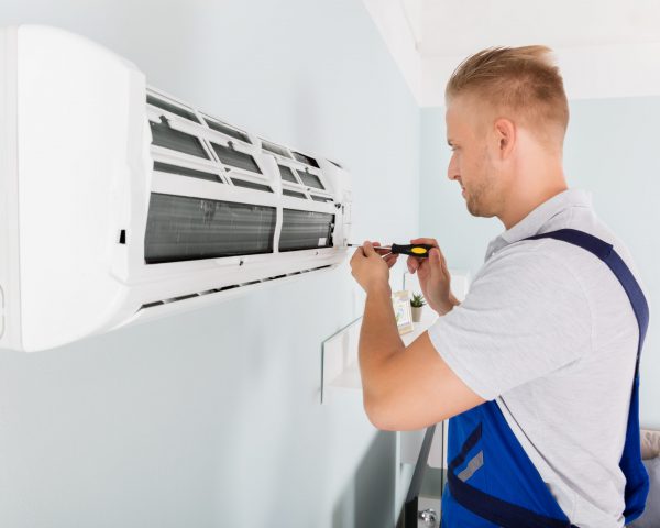 Young Male Technician Fixing Air Conditioner With Screwdriver
